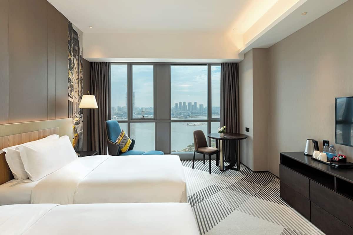 Une chambre d’hôtel avec deux lits, un bureau, une chaise, une télévision et une vue sur la ville.