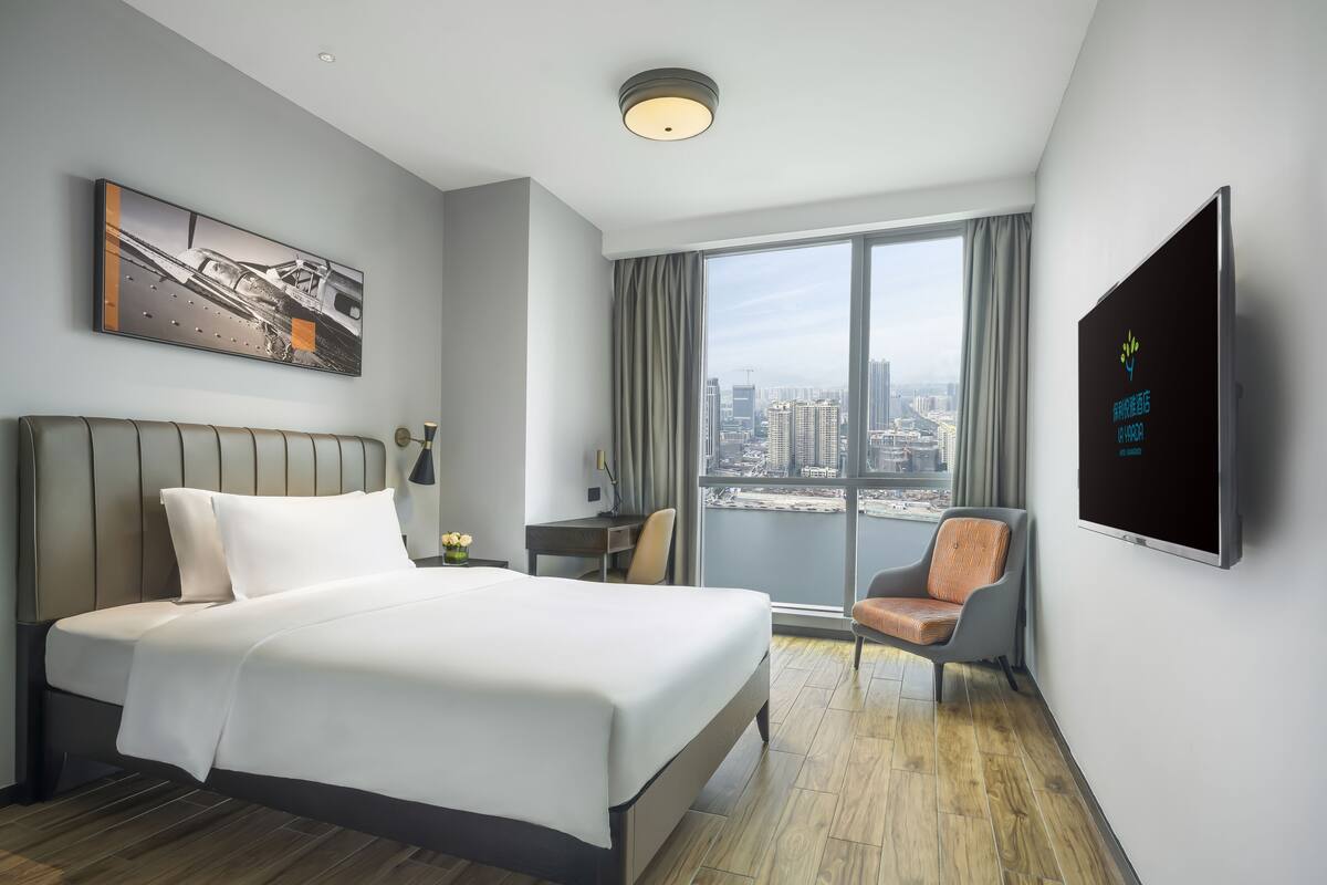 Une chambre d’hôtel moderne dotée d’un grand lit, d’un bureau, d’une chaise, d’une télévision et offrant une vue sur la ville.
