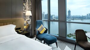 A hotel room with a large window, a bed, a desk with a lamp, and two chairs. - La Yarda Hotel Guangzhou - Free Shuttle Bus Available during Canton Fair Period (Guangzhou)