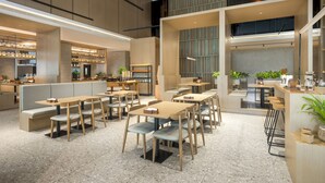 A modern cafe with multiple seating areas, including booths and tables, and a visible kitchen area. - La Yarda Hotel Guangzhou - Free Shuttle Bus Available during Canton Fair Period (Guangzhou)