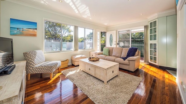 Un salon spacieux avec un plancher en bois, un canapé beige, un fauteuil à motifs et une table basse.