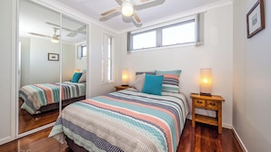 Une chambre avec un grand lit, deux tables de chevet, un ventilateur de plafond et une fenêtre.