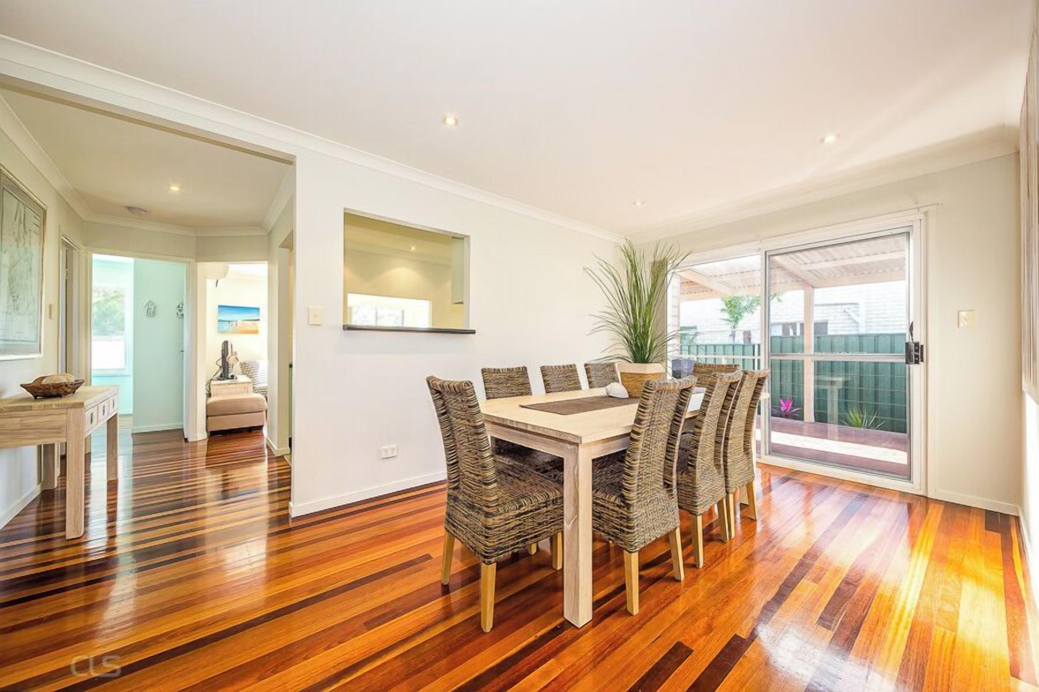 A dining area with a wooden table and wicker chairs, a potted plant, and a sliding glass door leading to a balcony.
