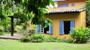 A yellow building with blue shutters, surrounded by lush greenery and stone pathways.
