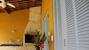 A room with a brick fireplace, a ceiling fan, and a vase with flowers on a table.