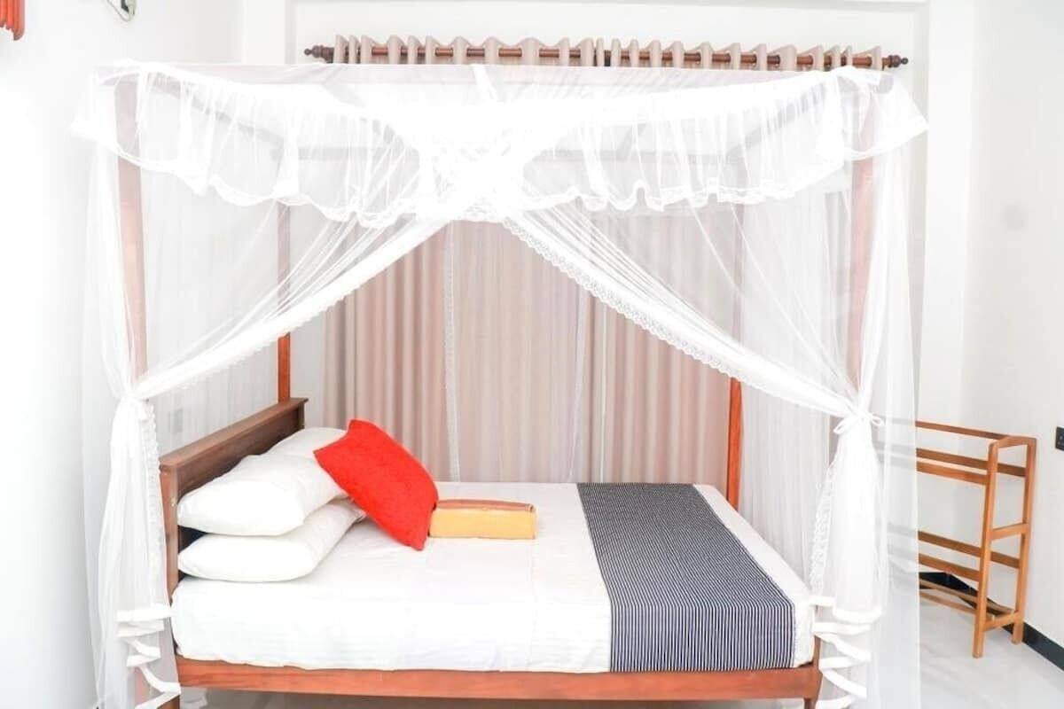 A bed with a white canopy, a red pillow, and a striped blanket.