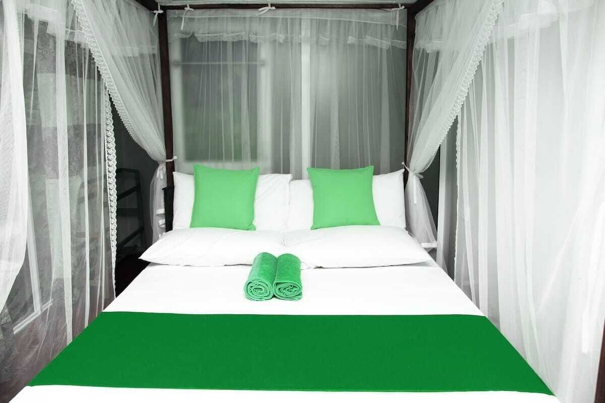 A bed with white and green bedding, a green throw blanket, and a canopy.