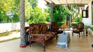 A covered outdoor seating area with wooden furniture and a table, surrounded by lush greenery. - Villa Serenity (Weligama)