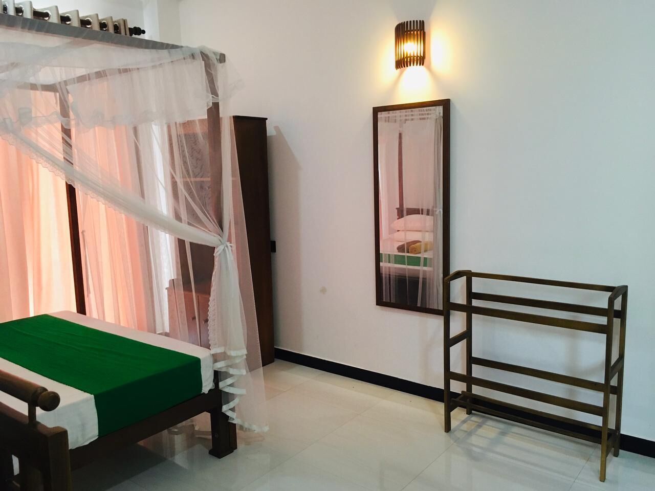 A bedroom with a bed, a bedside table, a nightstand, a wall-mounted lamp, and a mirror.