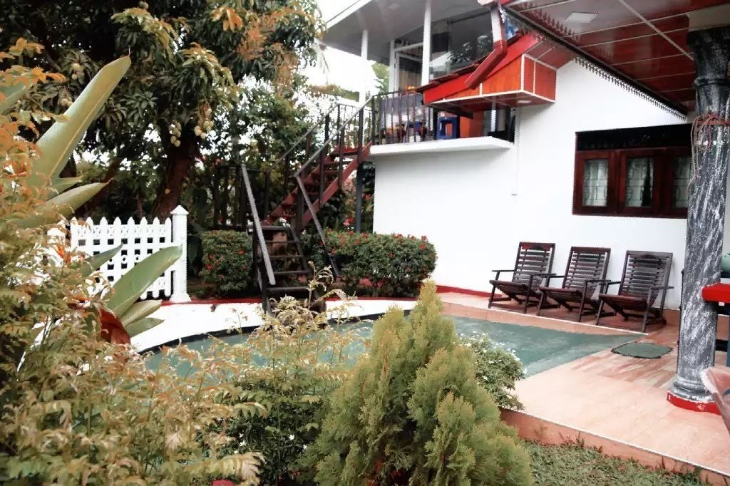 A white building with a red roof, a staircase, and a pool area with lounge chairs.