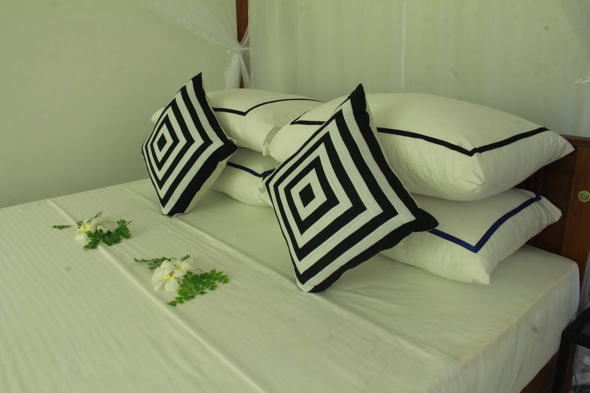 A neatly made bed with white linens and black and white patterned pillows, a small plant, and a wooden headboard.