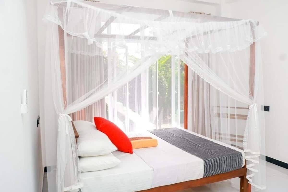 A bed with a canopy, white pillows, a red pillow, and a grey blanket.