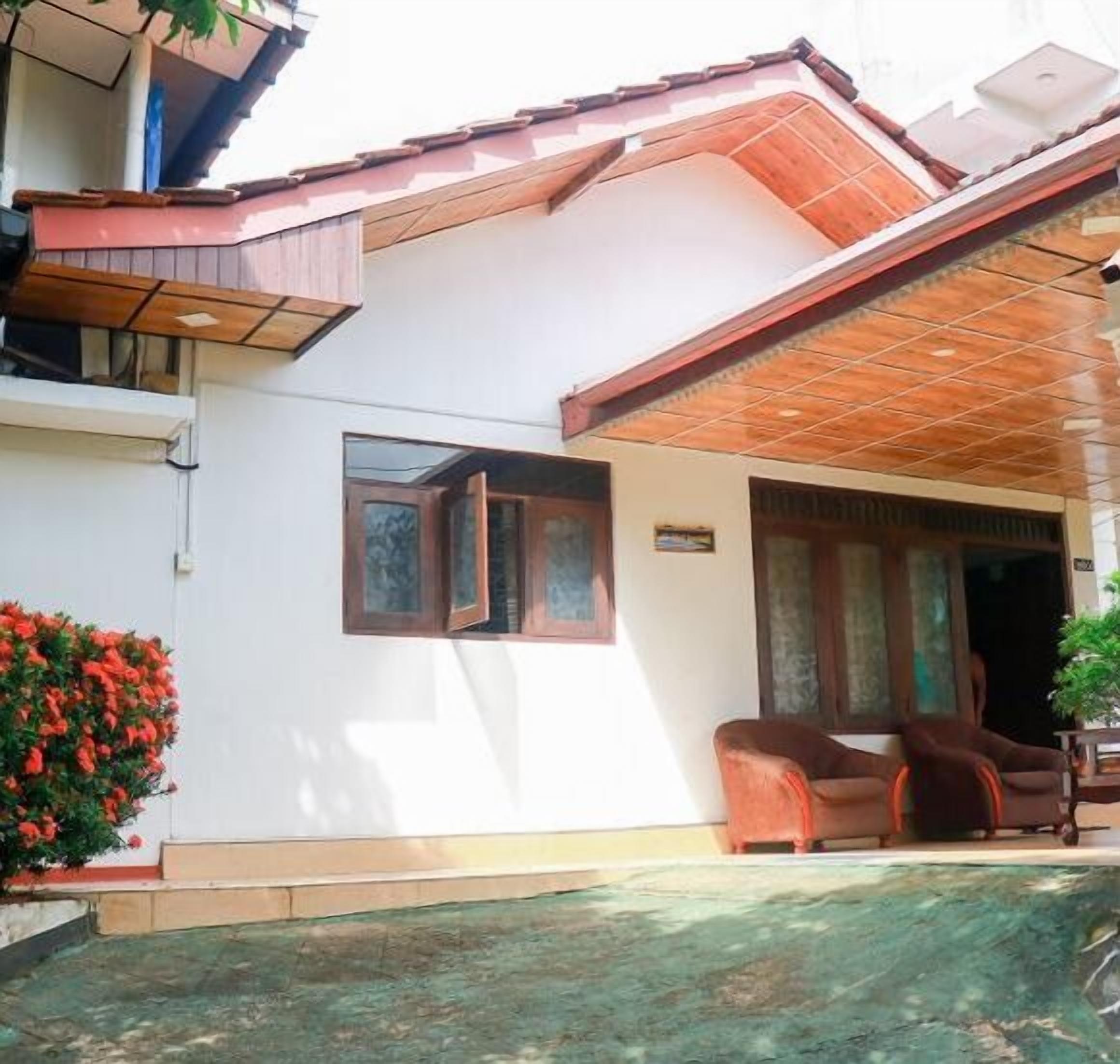 A two-story house with a tiled roof, a small balcony, and a swimming pool in the foreground.