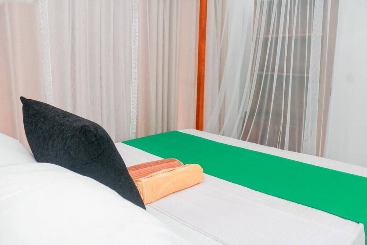 Un lit bien fait, avec une couverture verte, un oreiller noir et un livre orange plié.