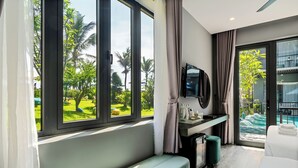 Ein modernes Hotelzimmer mit großem Fenster, einem Bett, einem Schreibtisch mit Spiegel und Blick auf einen Pool und Grünflächen.