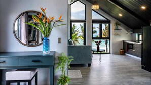 Ein modernes Wohnzimmer mit einem großen Fenster, einer blauen Vase mit Blumen, einem grauen Sofa und einem Essbereich.