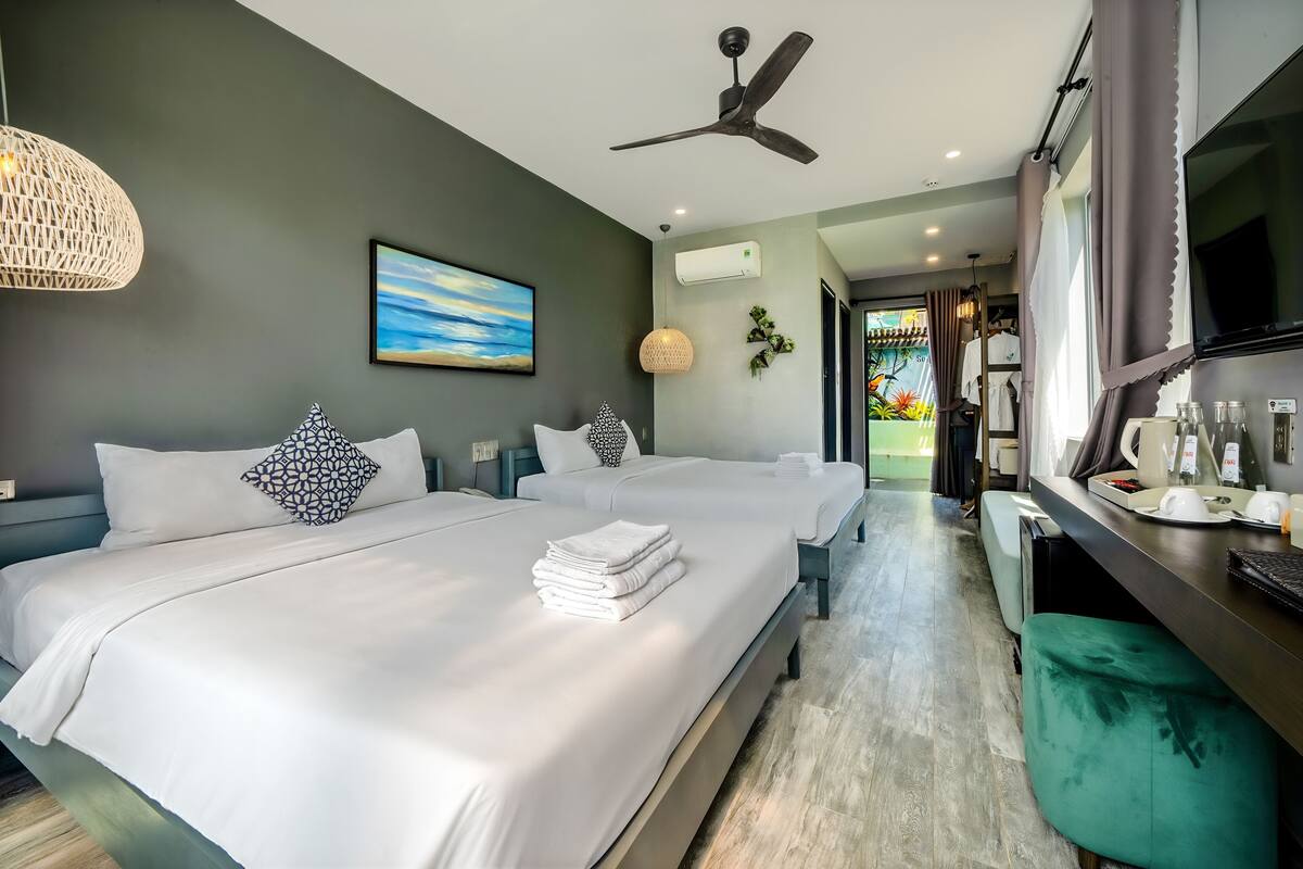 Une chambre d’hôtel avec deux lits, un bureau, une télévision et un ventilateur de plafond.