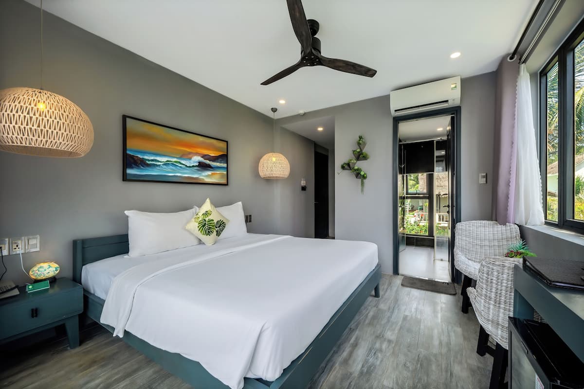 Une chambre moderne dotée d’un grand lit, d’un ventilateur de plafond, d’un climatiseur mural et offrant une vue sur l’extérieur grâce à une porte vitrée.