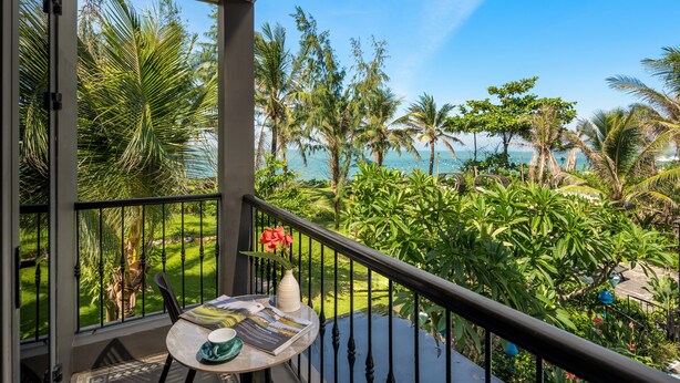 Ein Balkon mit Blick auf einen tropischen Garten und den Ozean.