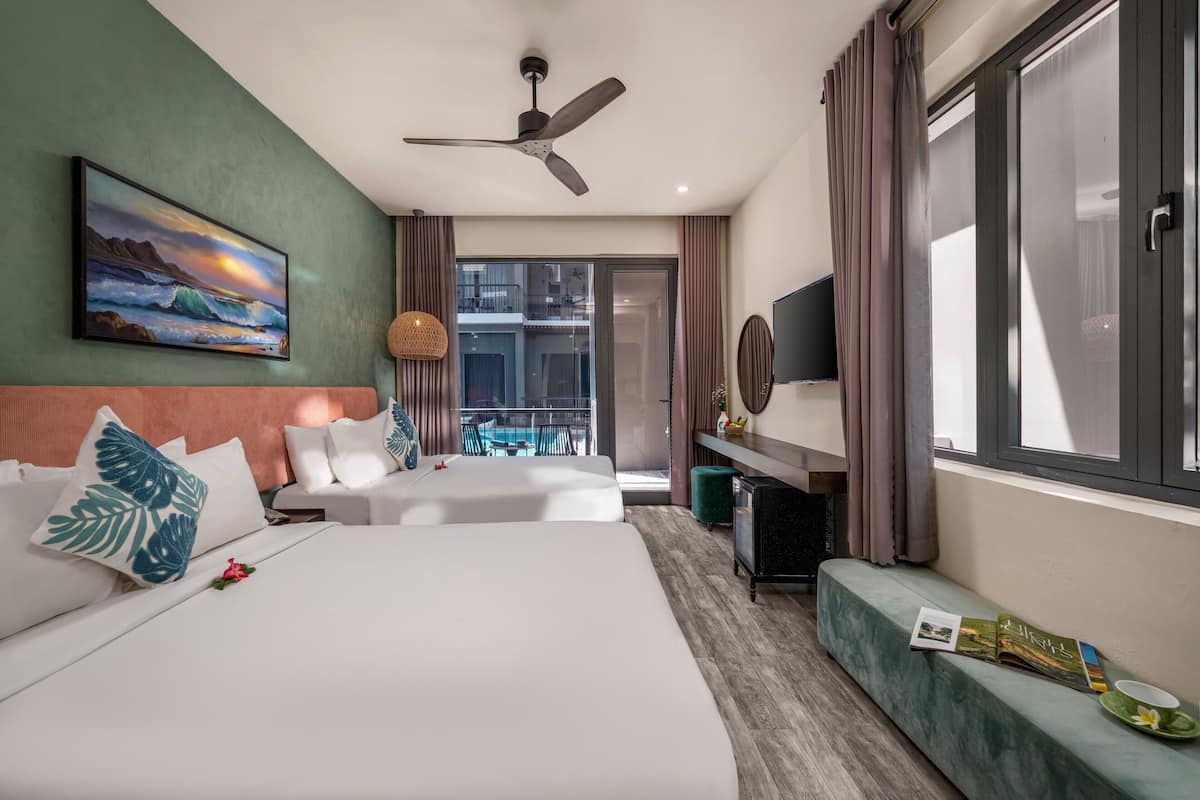 Une chambre d’hôtel avec deux lits, un ventilateur de plafond, une grande fenêtre avec des rideaux, un balcon donnant sur une vue agréable et un bureau avec une chaise.