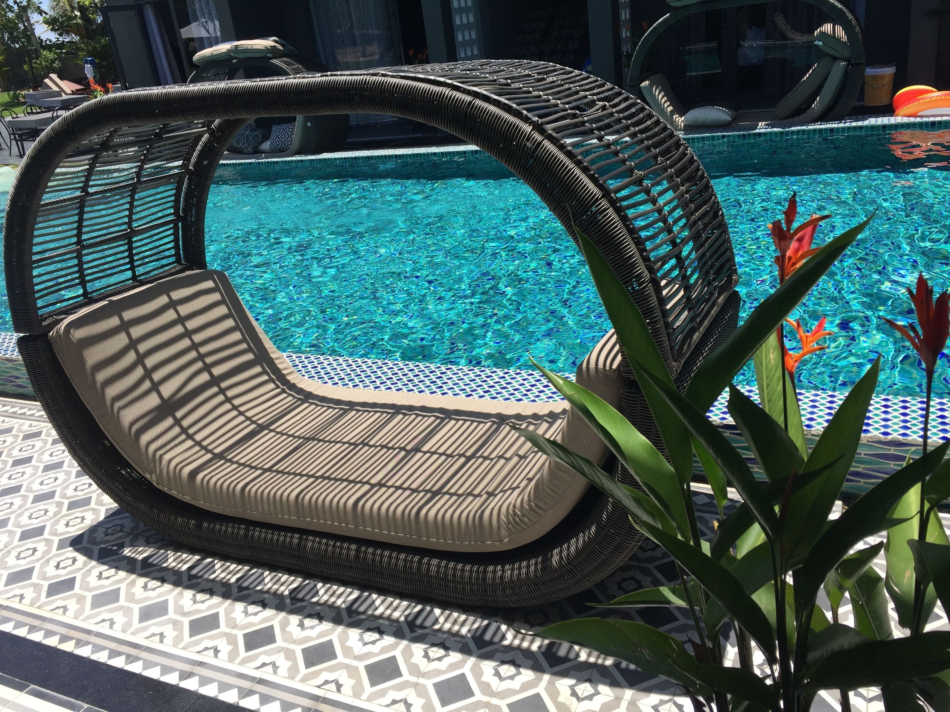 Un fauteuil de relaxation en osier placé près d’une piscine, sur un sol à motifs.