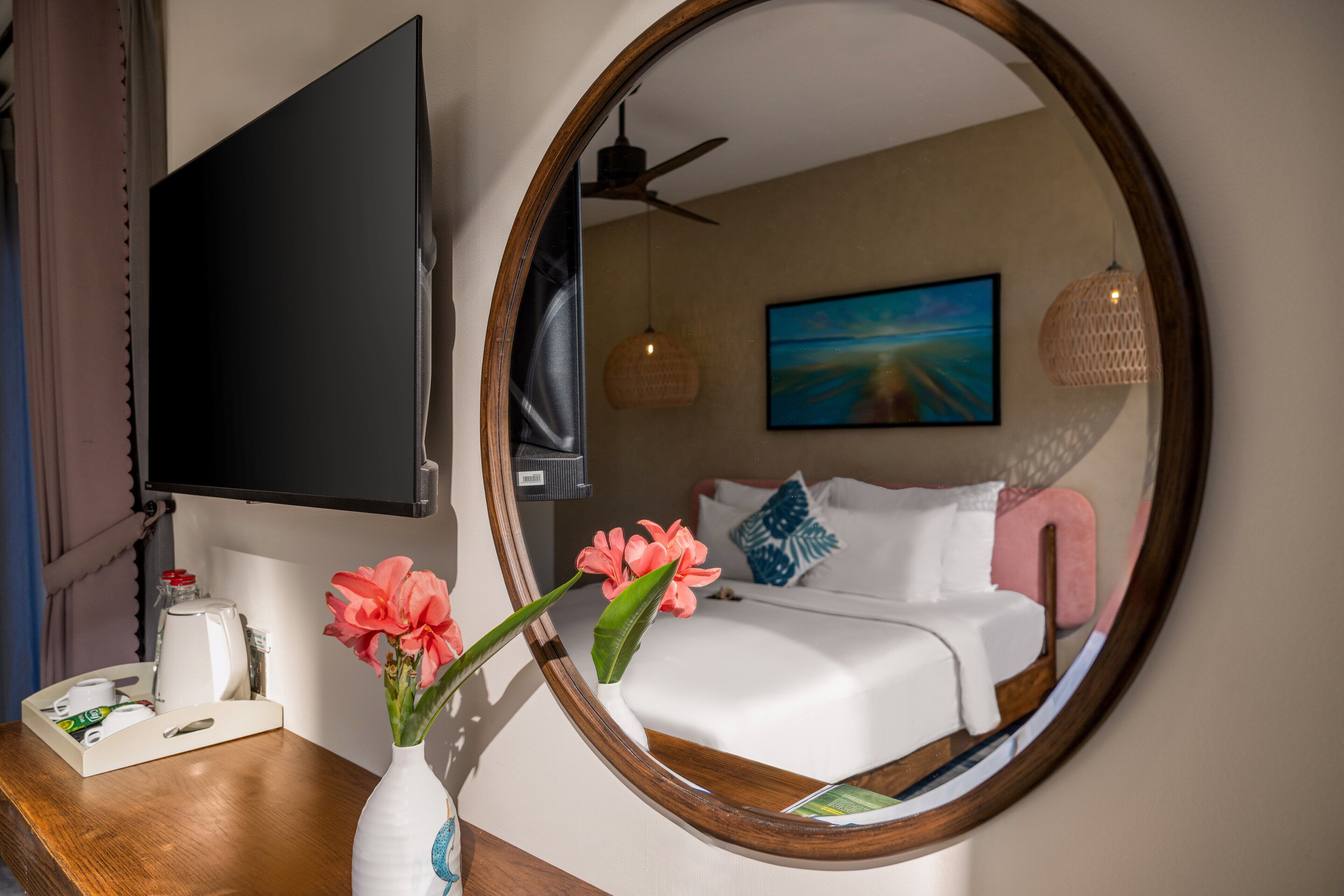 A hotel room with a bed, a TV, a mirror, a coffee maker, and a vase with flowers.