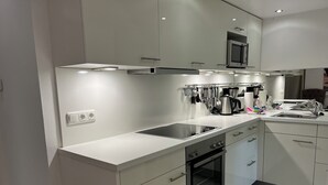 Een moderne keuken met witte kasten, een inbouwoven, een magnetron en een roestvrijstalen spoelbak.
