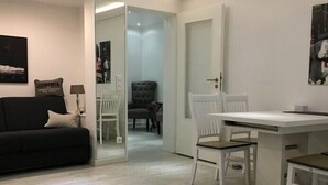 Een moderne woonkamer met een zwarte bank, een eettafel met witte stoelen en een grijze fauteuil.