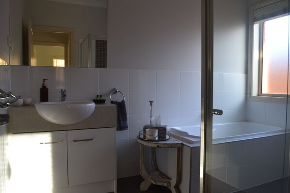 A bathroom with a white sink, a mirror, a bathtub, and a small table with toiletries. - Gone to Barossa | Stylish 3BR Retreat Walk to Wineries, Dining & Shops (Tanunda)