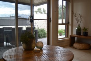 A room with a round wooden table, two potted plants, and a view of a patio area with outdoor furniture. - Gone to Barossa | Stylish 3BR Retreat Walk to Wineries, Dining & Shops (Tanunda)