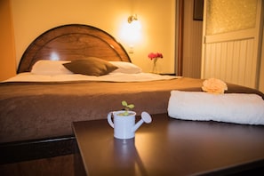 A neatly made bed with a wooden headboard, a bedside table with a white mug and a small plant, and a vase with pink flowers. - Samary Hostel (Puno)