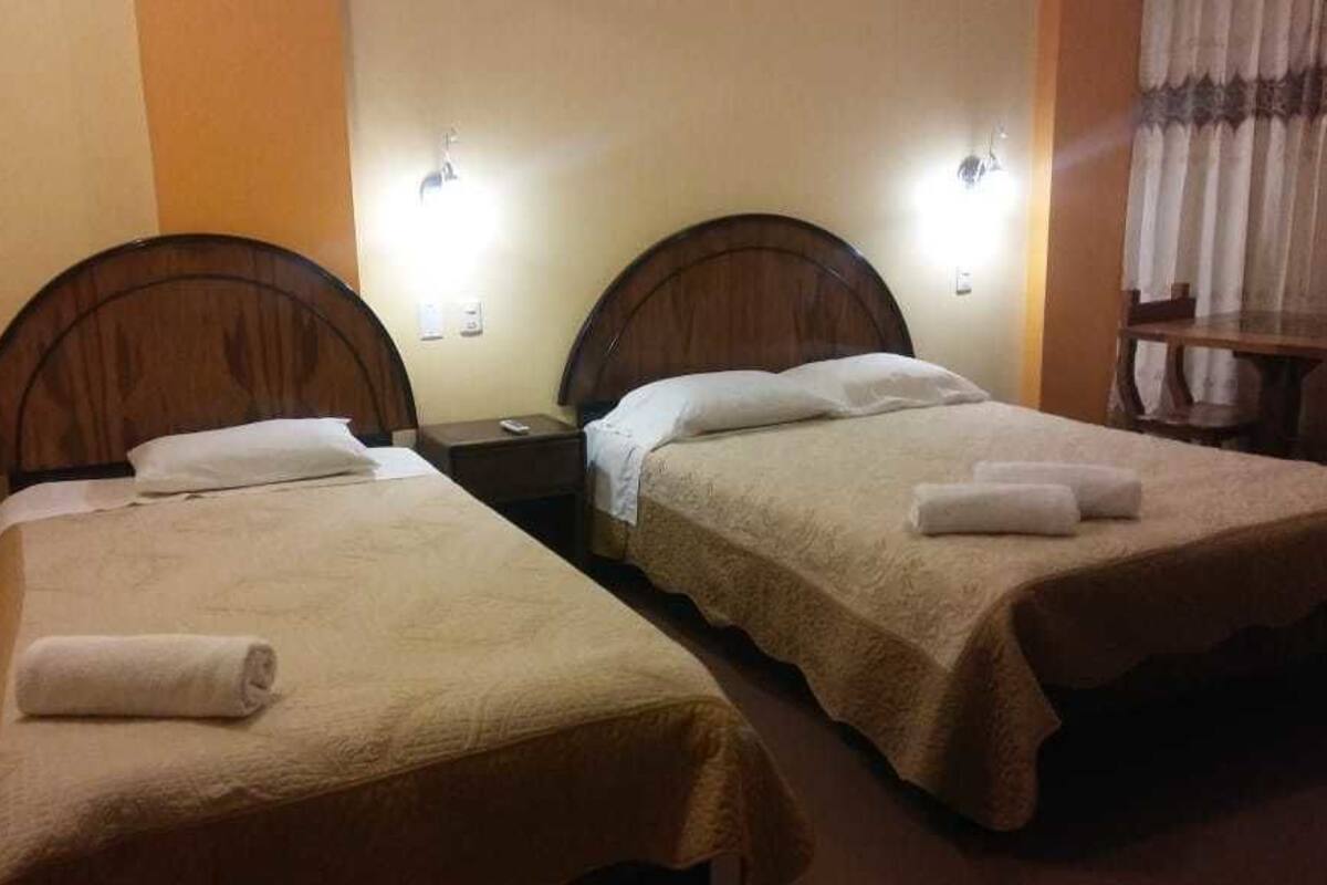 A hotel room with two single beds, each with a headboard, bedside tables, and lamps.