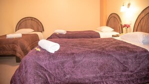 A hotel room with two beds, each with a headboard and pillows. There is a nightstand with a lamp and a vase with flowers. - Samary Hostel (Puno)