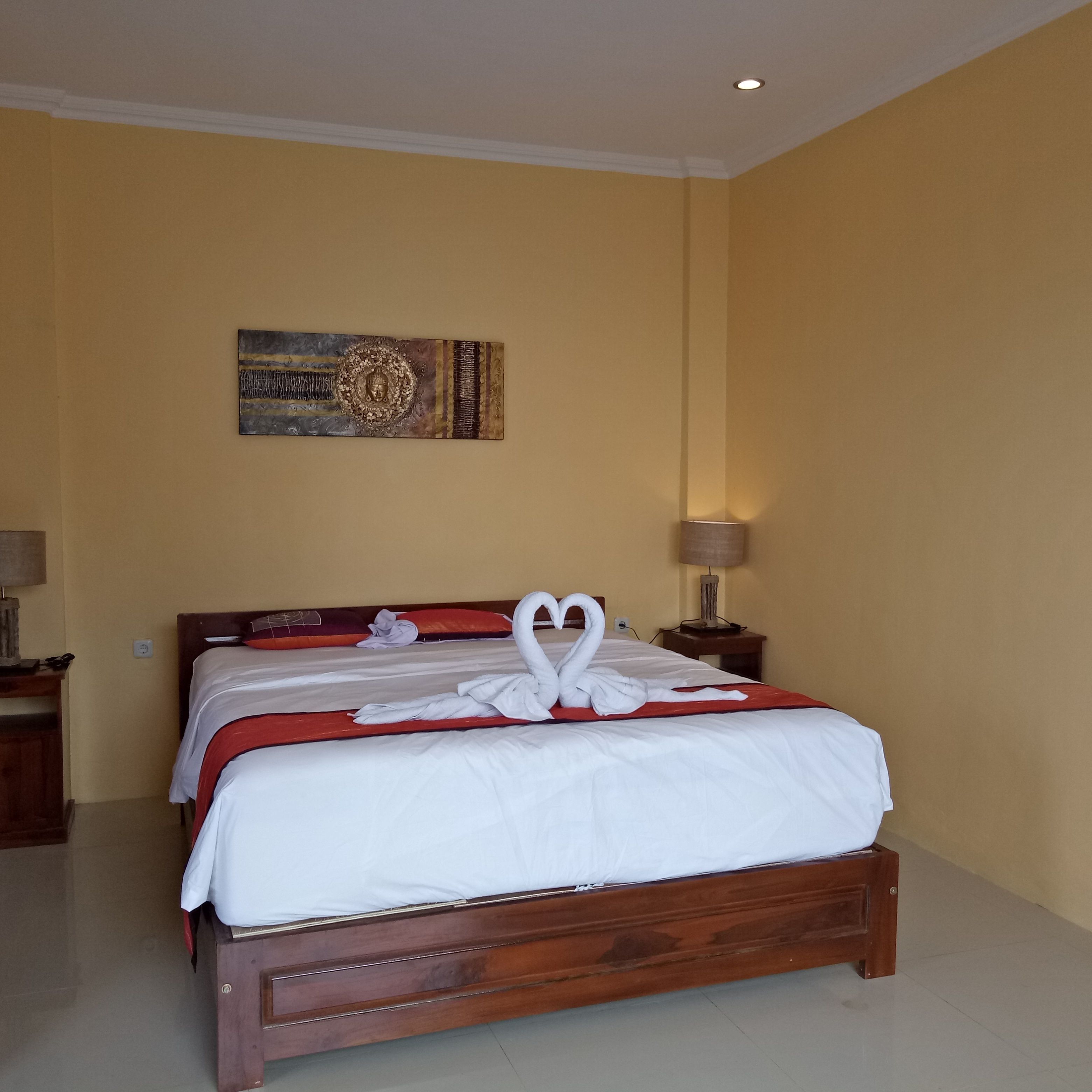 A hotel room with a wooden bed, a painting on the wall, and a lamp on the nightstand.