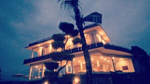 A multi-story house with a balcony, large windows, and a palm tree in front. - Atres Sari Resort (Munduk)