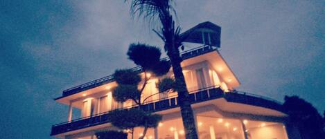 A multi-story house with a balcony, large windows, and a palm tree in front.