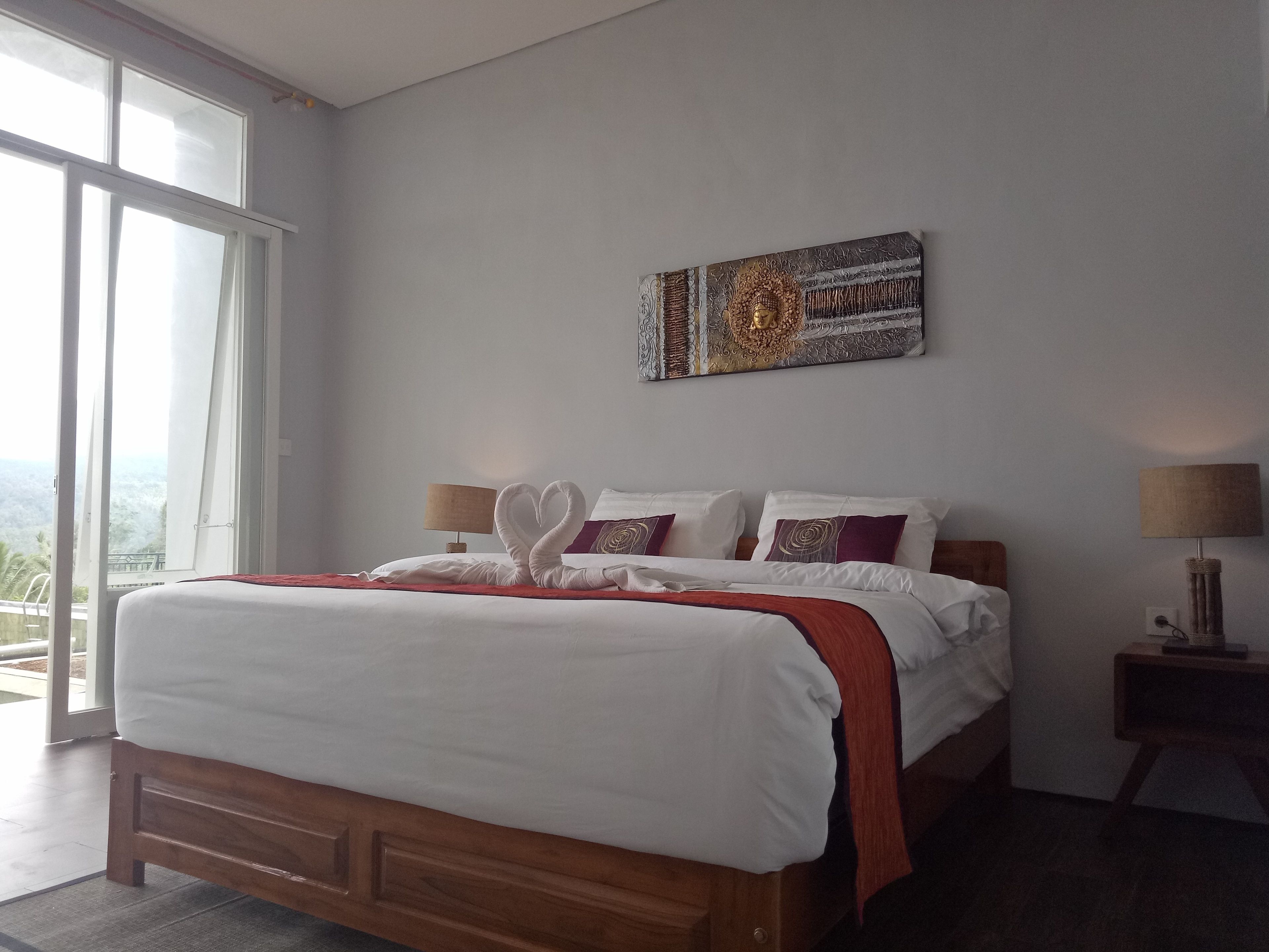 Ein Schlafzimmer mit einem großen Bett, Blick durch das Fenster und einem an der Wand befestigten Kunstwerk.