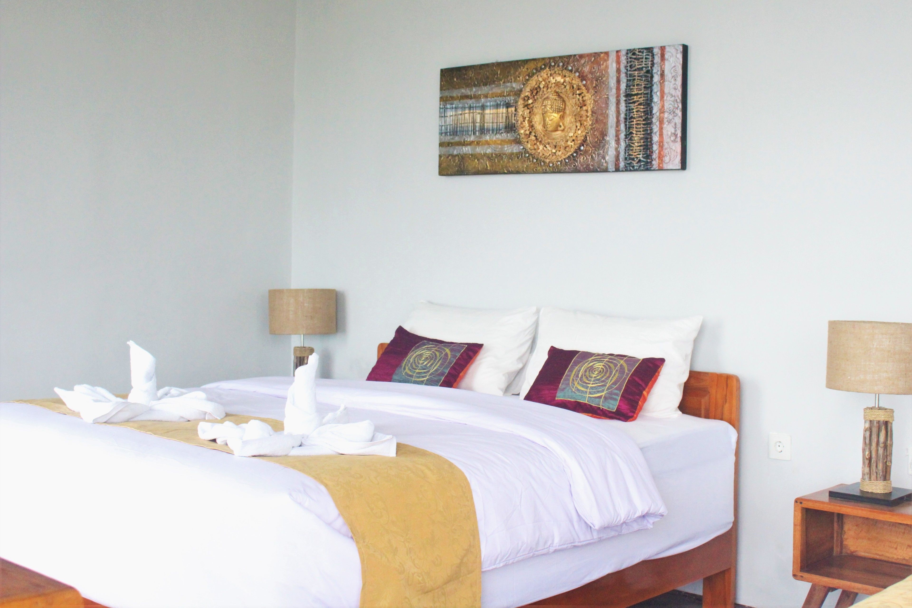 Una cama bien hecha con ropa blanca y un edredón dorado, dos almohadas y un adorno decorativo en la pared.