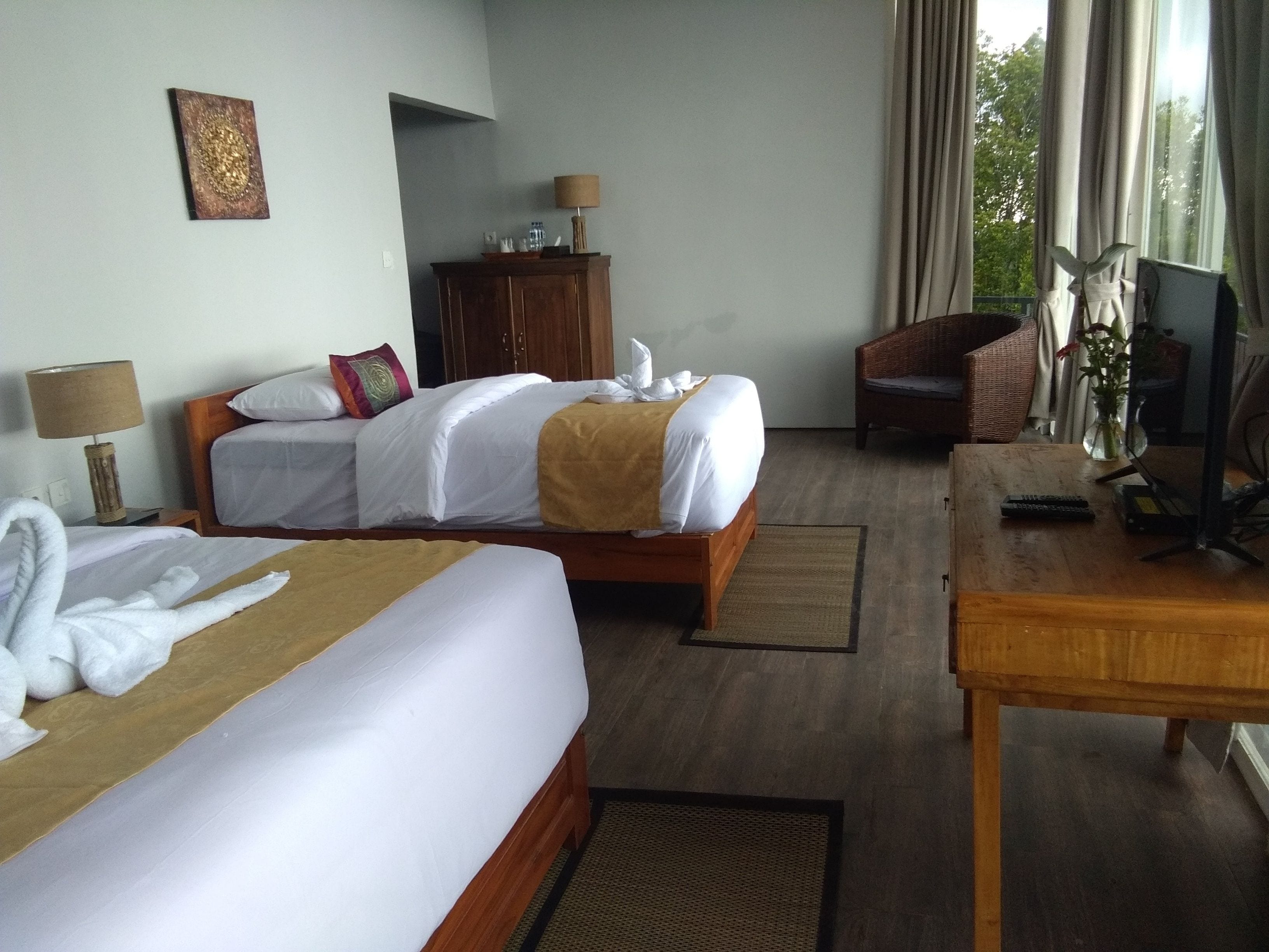 A hotel room with two beds, a wooden desk, a television, a lamp, a cabinet, and a window with curtains.