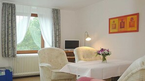Una habitación con dos sillones, una mesita con un jarrón de flores, una lámpara y un televisor.