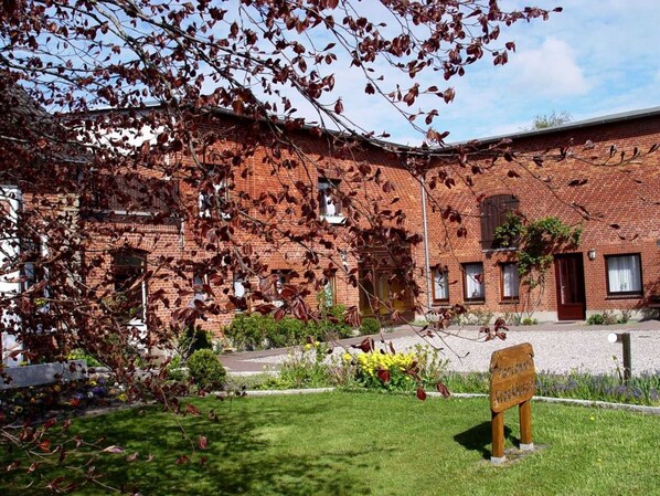 A brick building with a garden in front, a bench, and a sign.