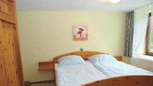 Una cama de madera con dos almohadas, una mesita de noche, un armario de madera y un cuadro en la pared.
