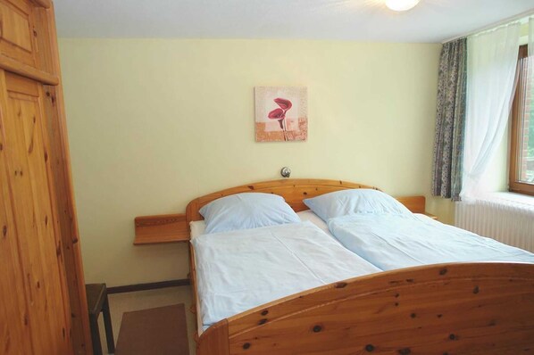 A wooden bed with two pillows, a nightstand, a wooden wardrobe, and a painting on the wall. - Ferienhof Jens vacation apartment 6 Falshöft (Kronsgaard)