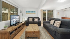 A modern living room with a large TV, two sofas, a wooden coffee table, and a view of the outdoors through large windows. - Serene Family Escape with Pool (WOORIM)