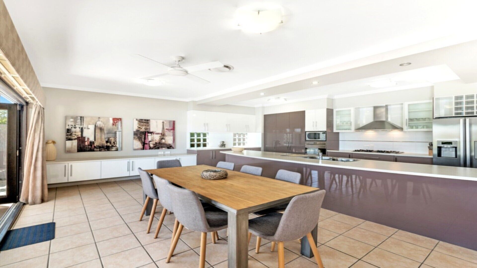 Een moderne keuken met een centraal eiland, witte kasten, roestvrijstalen apparatuur en een eethoek met een houten tafel en stoelen.