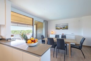 A modern kitchen with a fruit bowl, dining table, chairs, and a view through the window.