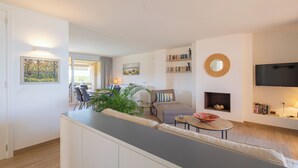 A modern living room with a sofa, a coffee table, and a fireplace. There is a television mounted on the wall and a bookshelf with books. - Frontline apartment with garden and pool. Parking . Capacity 4 Persons. WIFI (PALS)