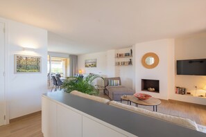 Een moderne woonkamer met een bank, een salontafel en een open haard. Een televisie is aan de muur bevestigd en er staat een boekenkast vol boeken.