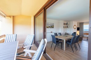 Una sala de estar moderna con comedor, una cocina al fondo y un amplio ventanal corredera que da a un balcón.