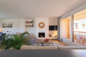 A modern living room with a sofa, coffee table, and a fireplace. There is a bookshelf and a TV mounted on the wall.